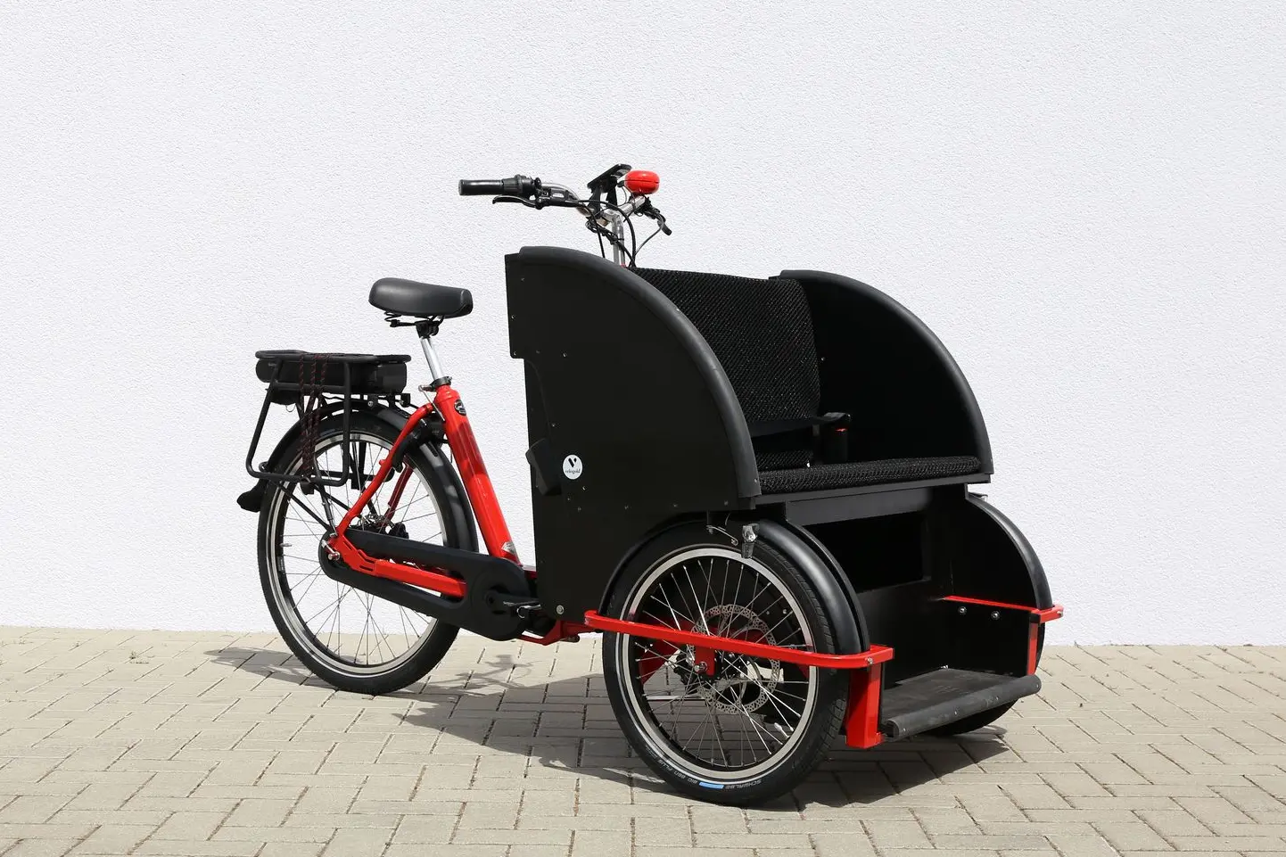 Bakfiets Rikscha: Komfortabel unterwegs mit Mitfahrer:innen. Bakfiets Rikscha vor einer Hauswand – bereit für die Beförderung von Senior:innen.