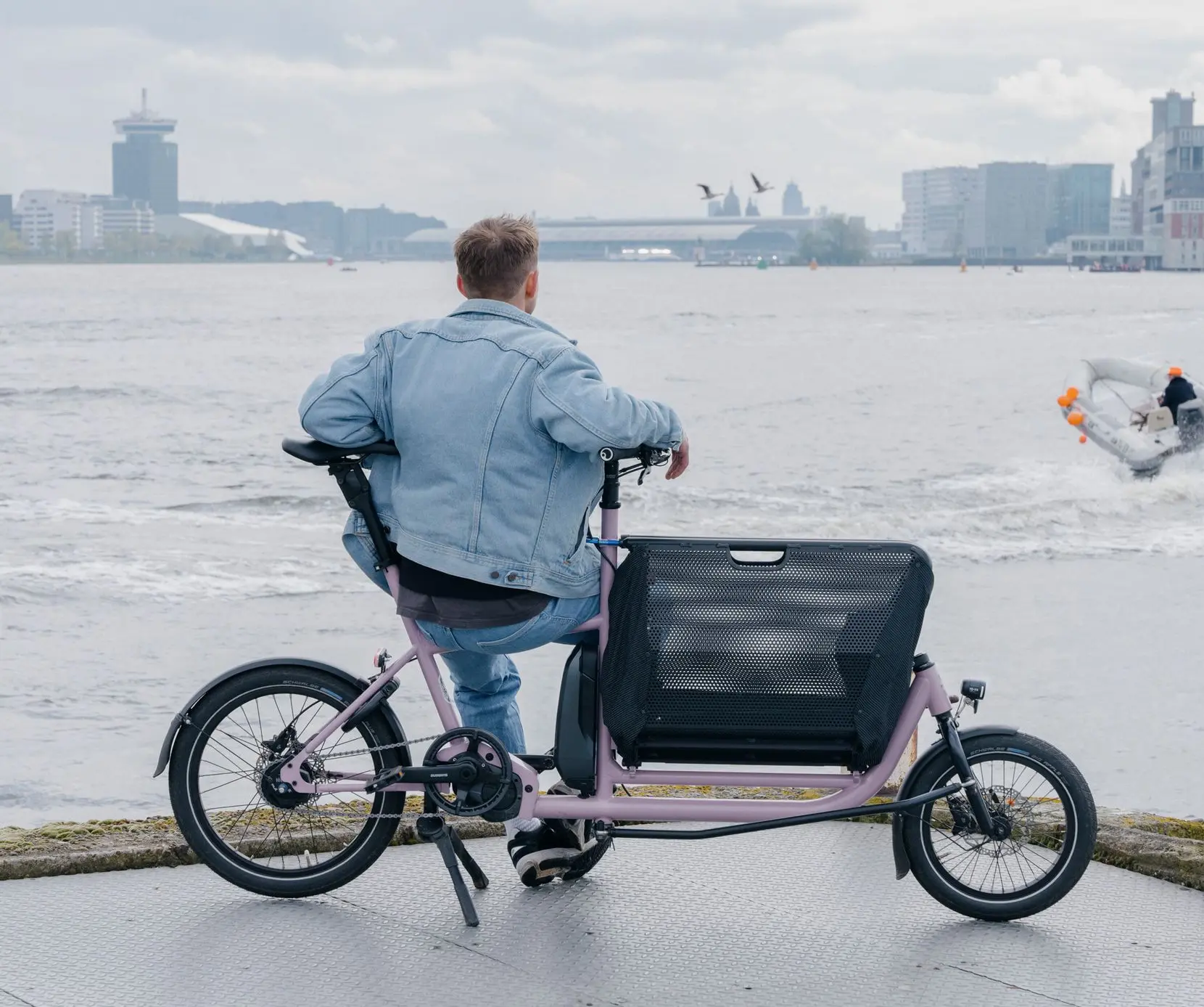 MULI Motor ST: dein entspannter Begleiter für Stadt, Küste und Alltag. MULI Motor ST Lastenrad – Mann sitzt entspannt auf dem Rad und blickt aufs Wasser, urbane Szenerie im Hintergrund.