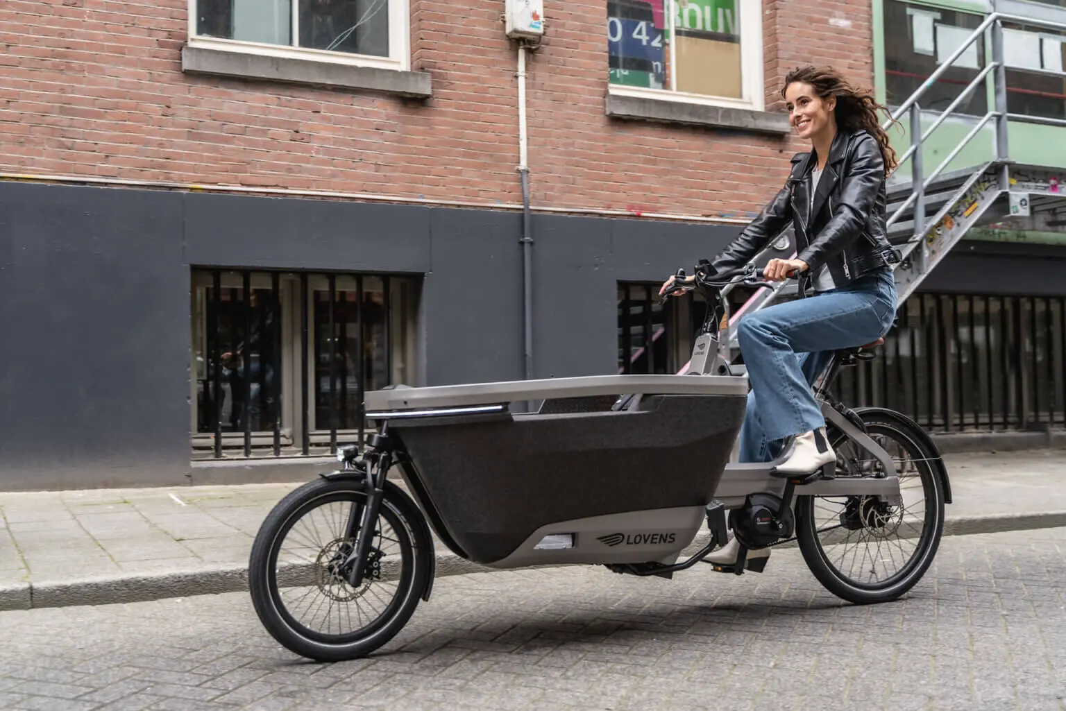 Lovens Lastenrad – sicher, stylisch und alltagstauglich für moderne Familien. Frau fährt ein Lovens Lastenrad durch ein Wohnviertel – vorne leer, unterwegs im Alltag.