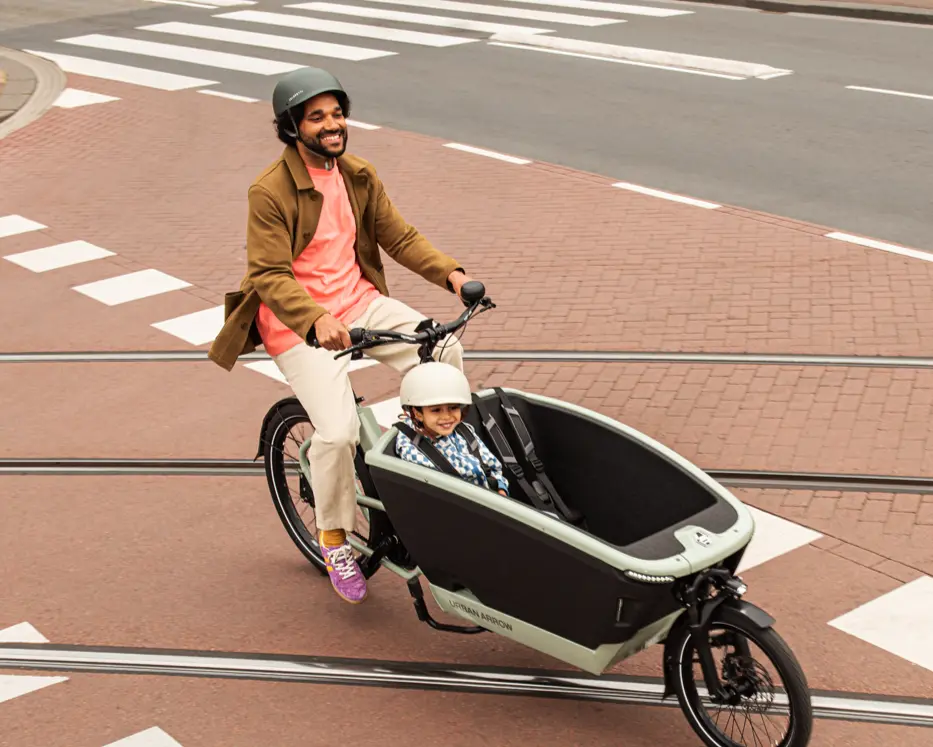 Fröhlicher Vater mit Kind unterwegs im Lastenrad – Fahrspaß und Familienmobilität vereint.